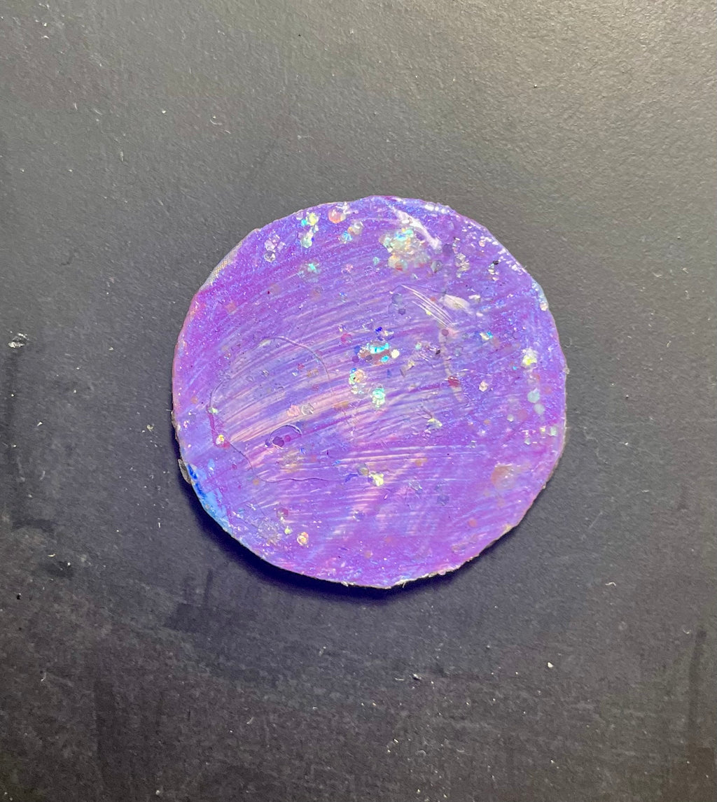 A round, purple iridescent charm magnet with a textured surface.