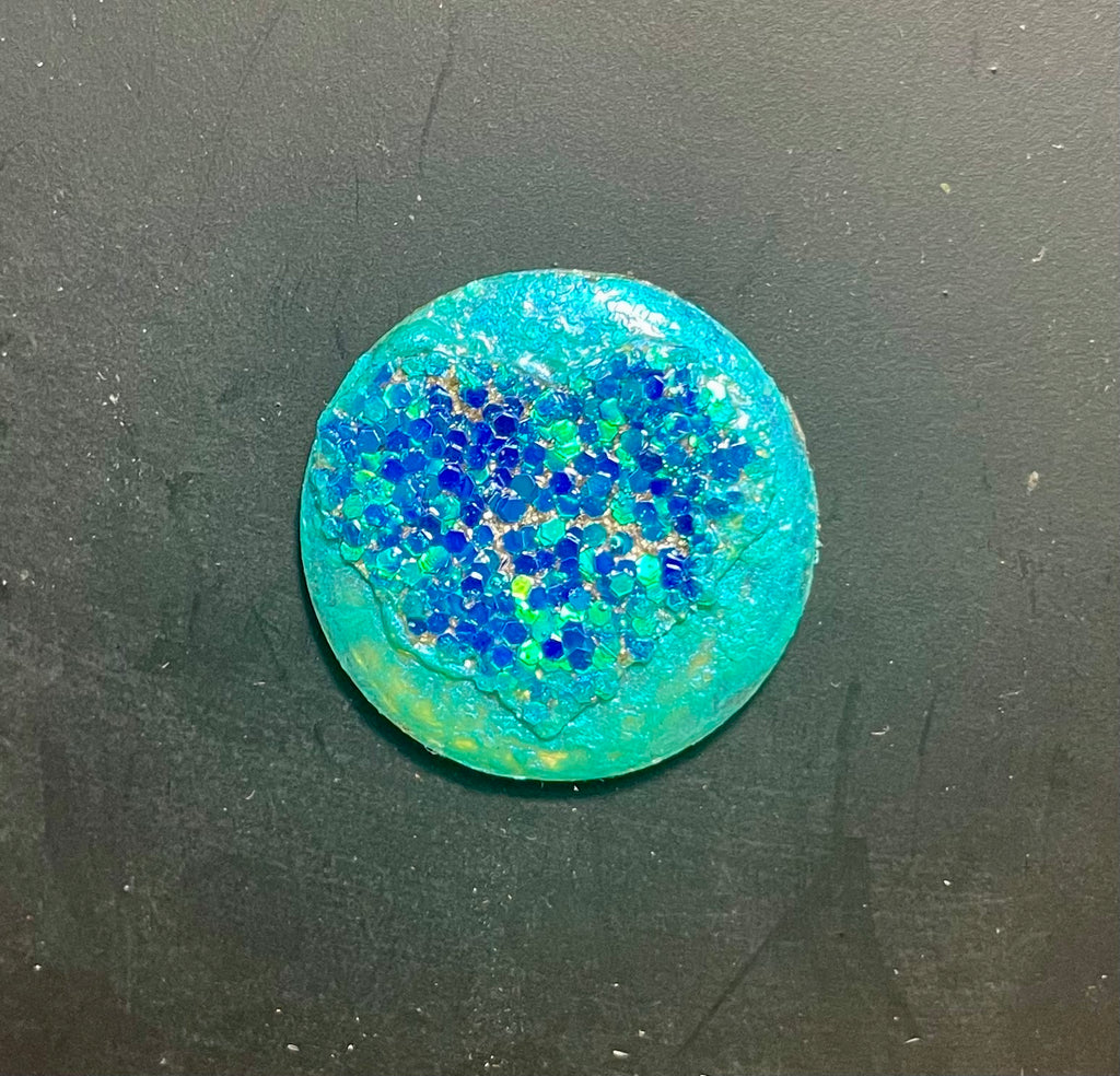 A round, blue resin magnet with a textured surface and glitter-like particles.