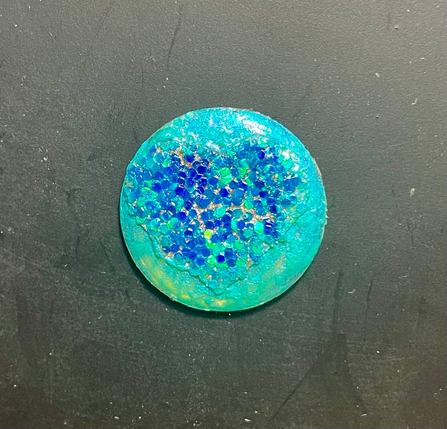 A round, blue resin magnet with a textured surface and glitter-like particles.
